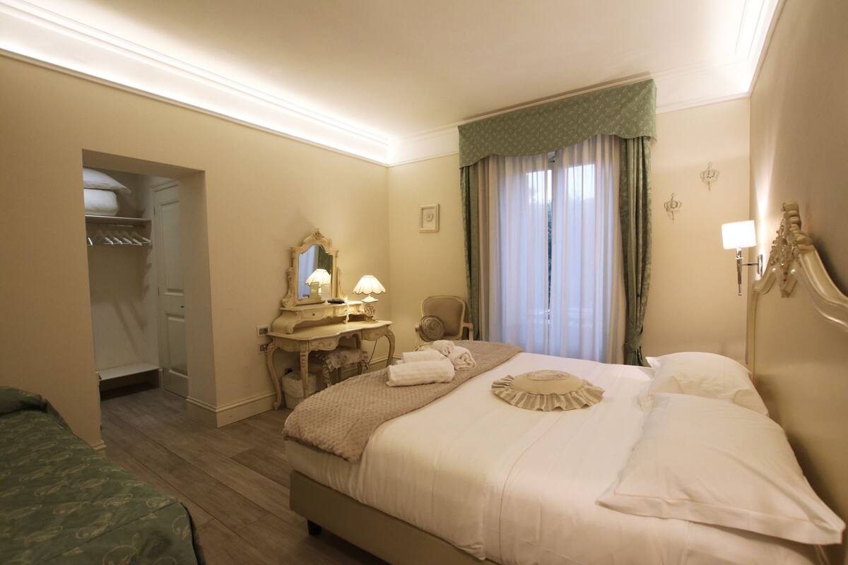 A hotel room with a large bed, a vanity with a mirror, a chair, and a walk-in closet.
