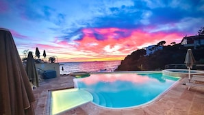 A pool area with a sunset view, stone flooring, and umbrellas. - Hotel Villa Margherita (Livorno)