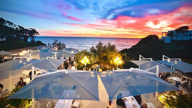A rooftop terrace with tables and umbrellas overlooking a sunset view. - Hotel Villa Margherita (Livorno)