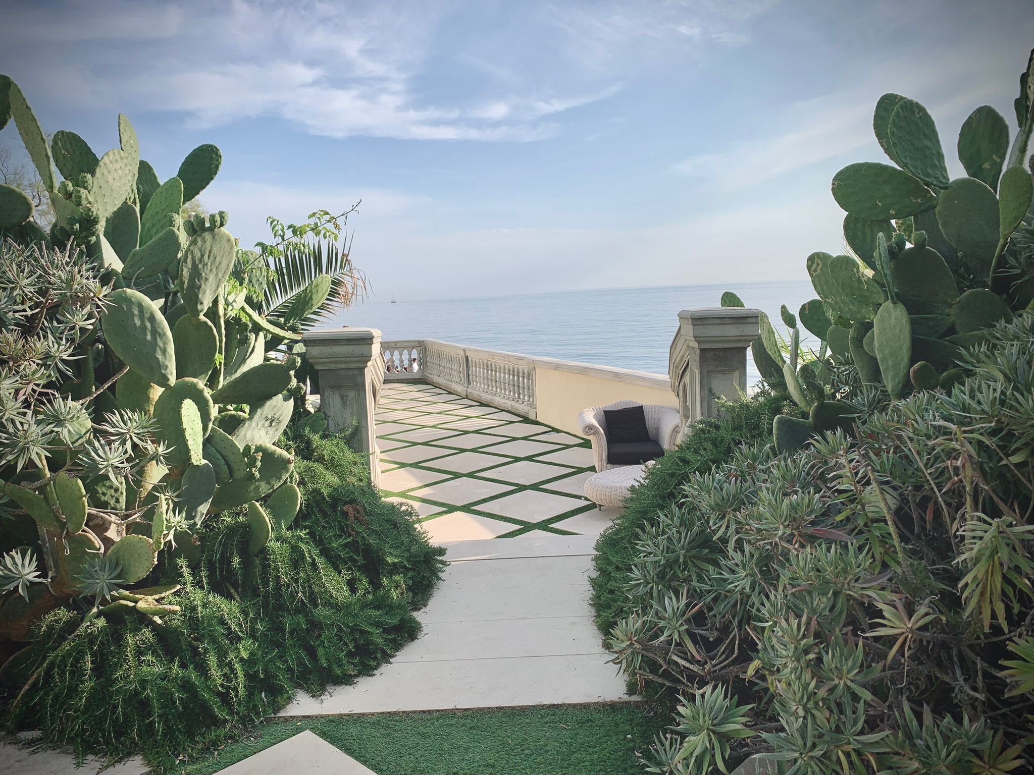 A pathway leading to a balcony overlooking the sea, surrounded by cacti and other greenery.