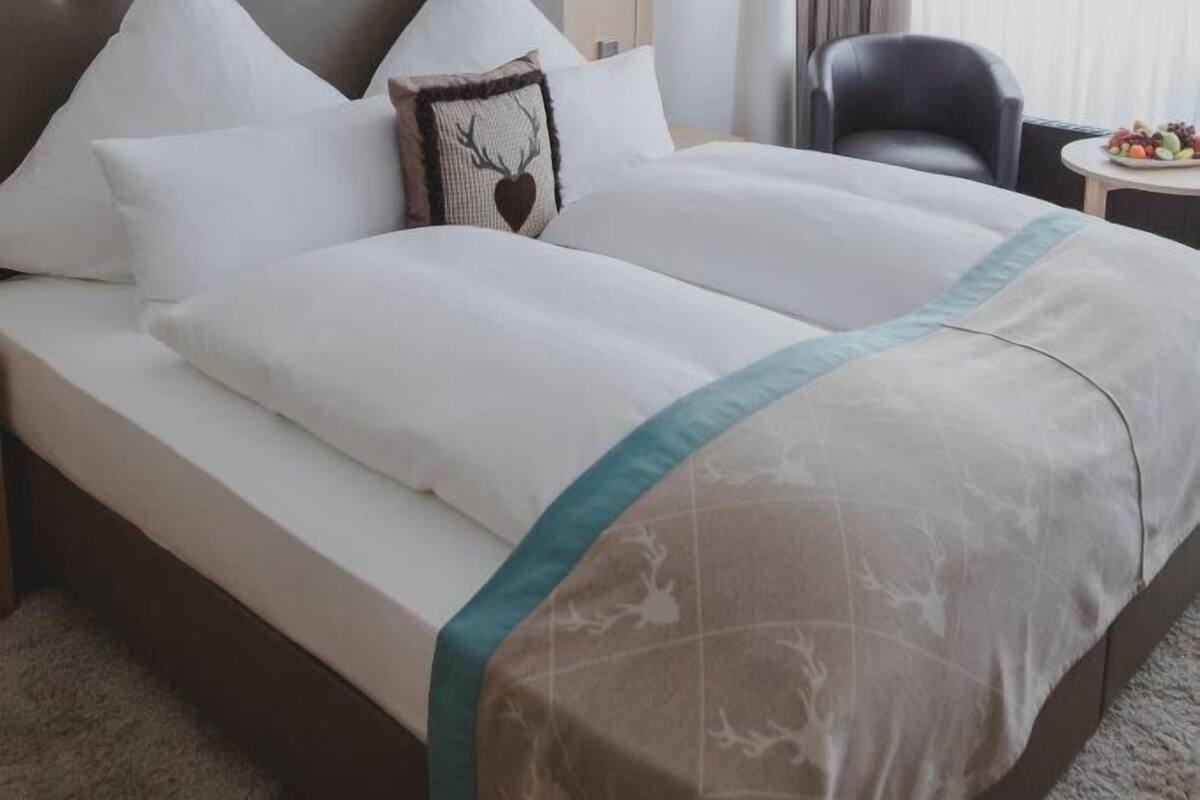 A hotel room with a large bed, a bedside table, a lamp, a chair, and a small table with fruit.