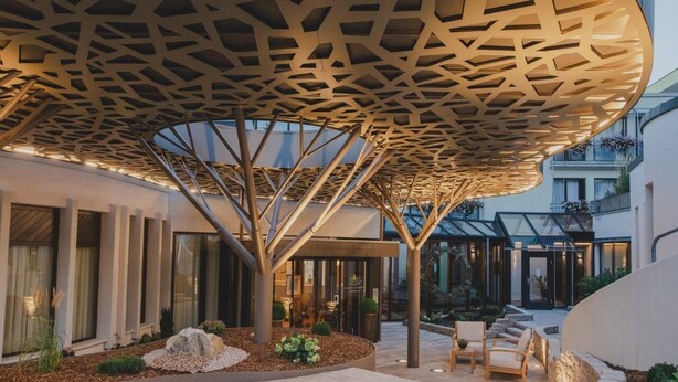 A modern building with a unique geometric ceiling structure, a landscaped outdoor area with seating, and a glass entrance. - Kunzmann's Hotel (Bad Bocklet)