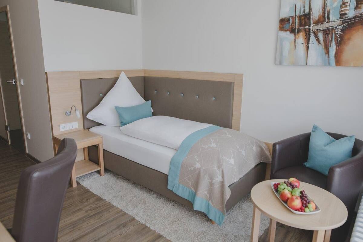 A modern hotel room with a bed, a small table with fruit, a chair, and a sofa.