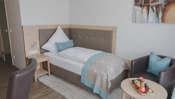Une chambre d’hôtel moderne avec un lit, une petite table sur laquelle se trouvent des fruits, une chaise et un canapé.