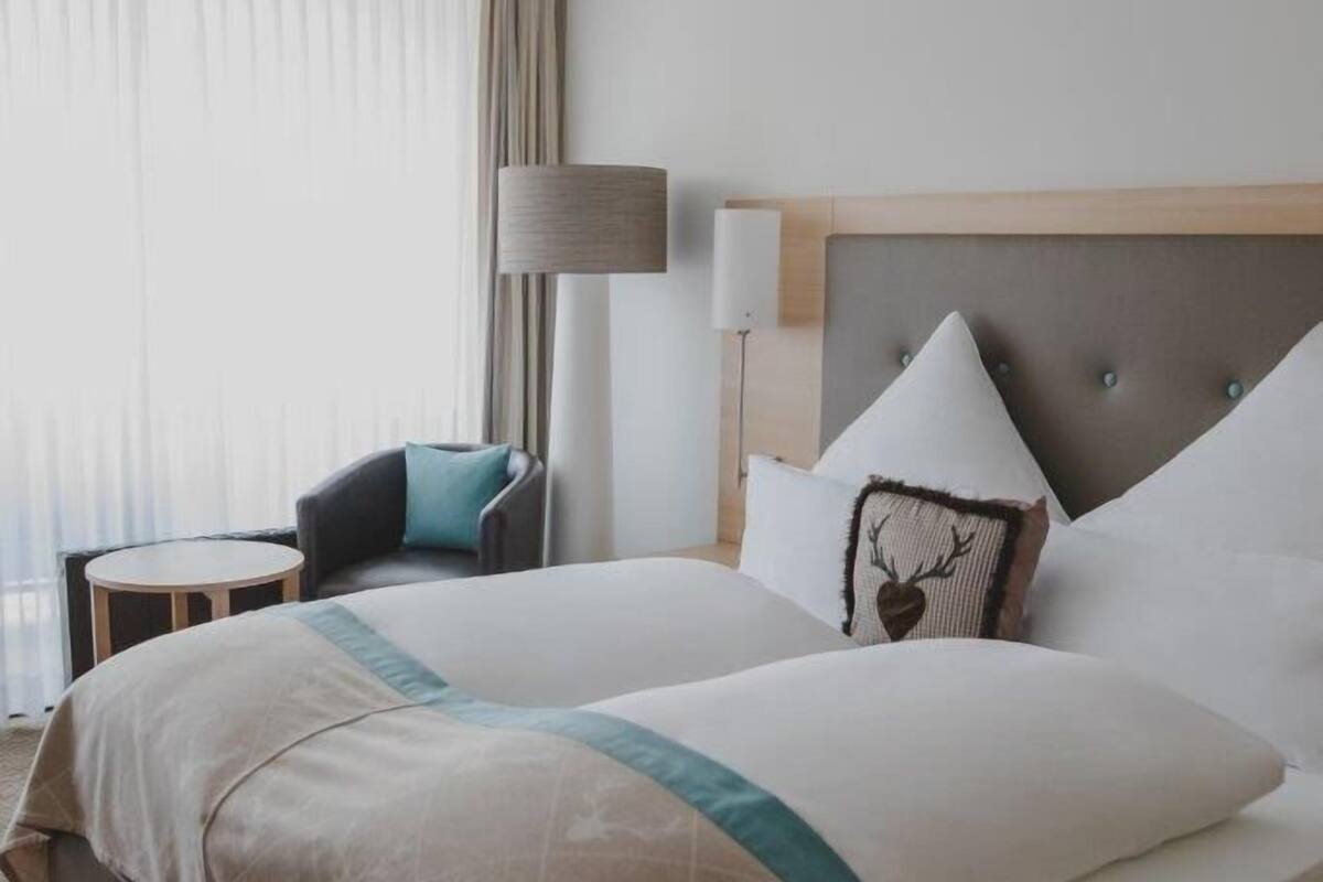A hotel room with a large bed, a chair, a lamp, and a view of the outdoors.