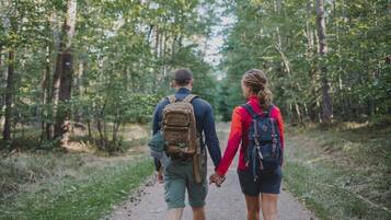 Two people walking on a forest path, each carrying a backpack.