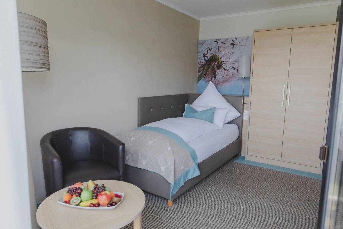 A hotel room with a bed, a chair, a small table with fruit, and a wardrobe.