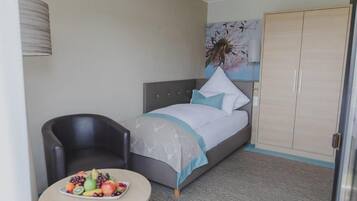 A hotel room with a bed, a chair, a small table with fruit, and a wardrobe.