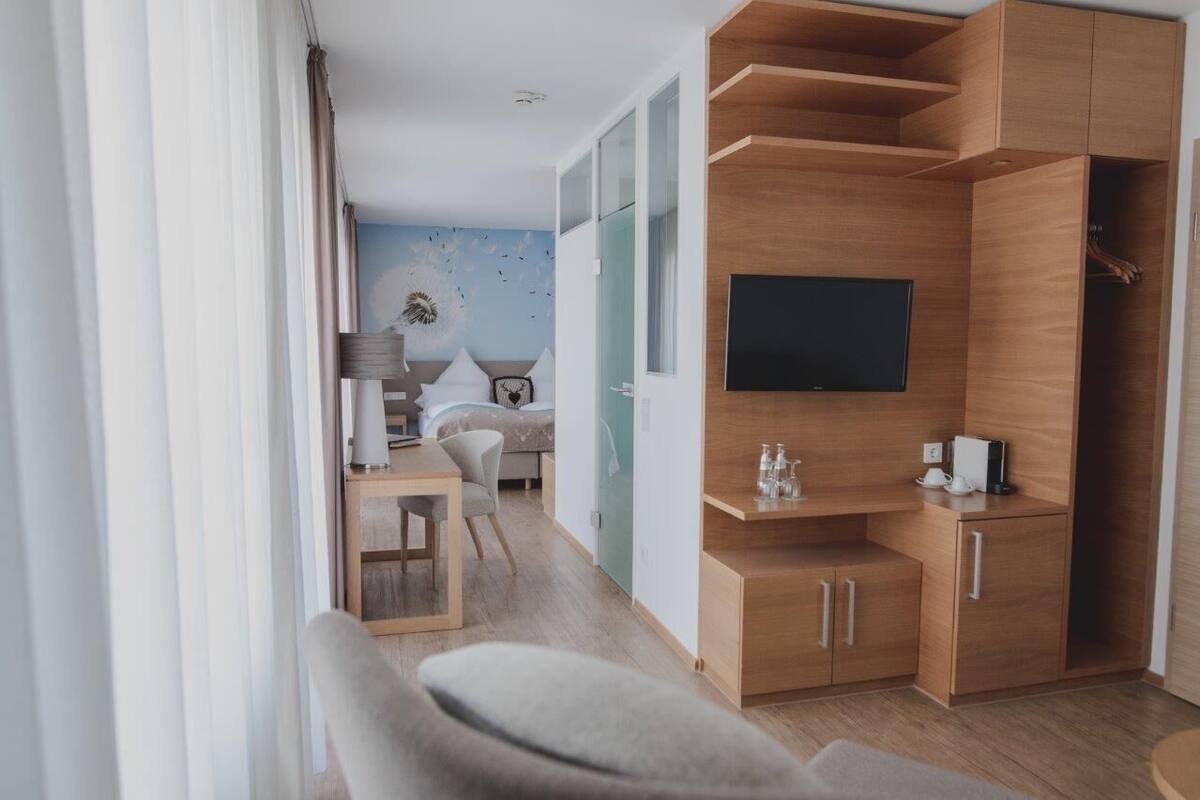 A modern hotel room with a wooden TV stand, a flat-screen TV, a small table with a lamp, and a bed with a blue wall mural.