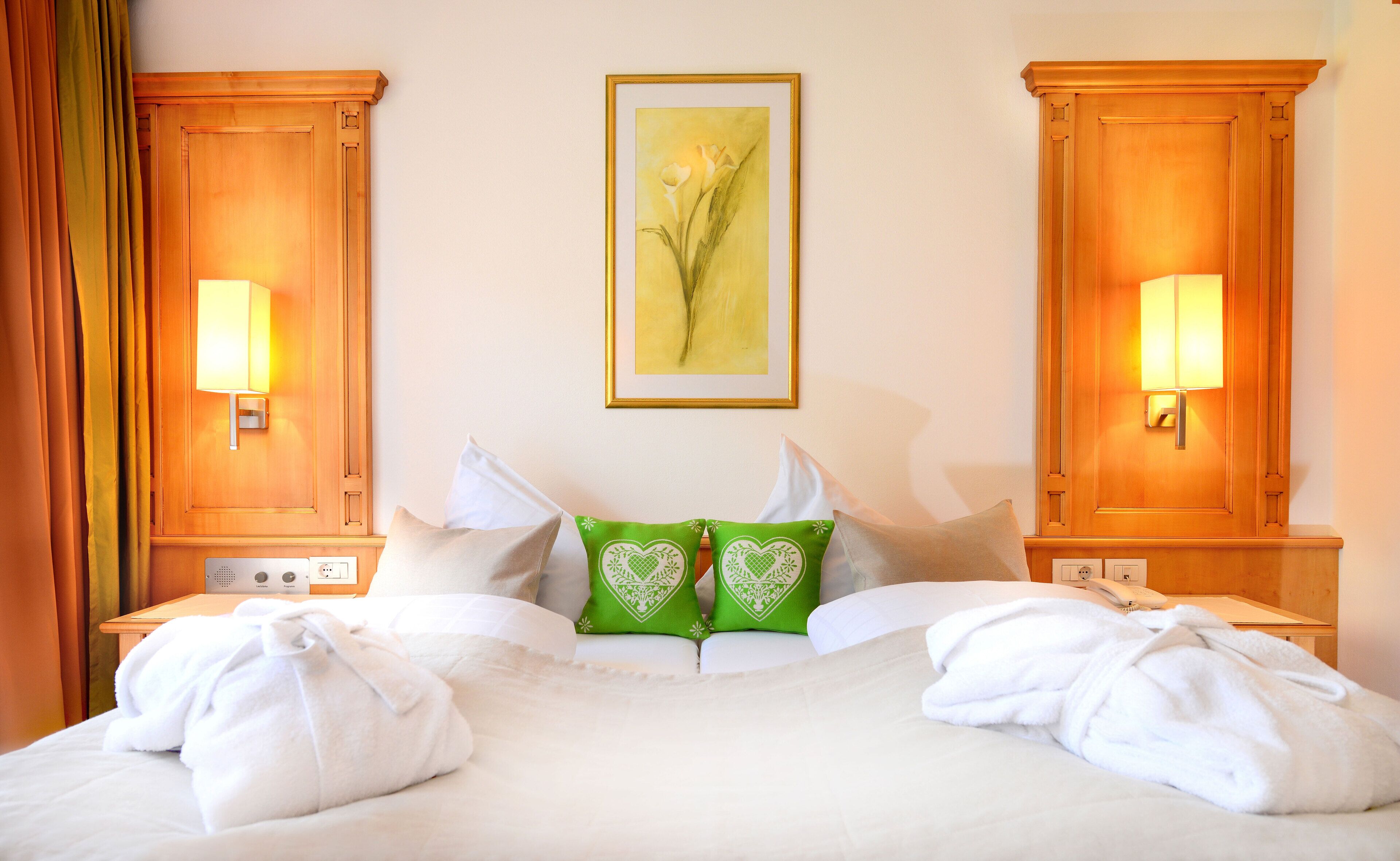Ein Hotelzimmer mit einem großen Bett, zwei Nachttischen, einem gerahmten Kunstwerk an der Wand und einem Fenster mit Vorhängen.