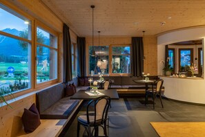 A cozy interior with wooden walls, large windows offering a view of the outdoors, and a seating area with tables and chairs. - Hotel Brunnerhof (Rasun Anterselva)