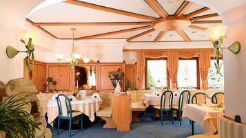 A dining area with wooden paneling, a high ceiling with exposed beams, and tables set for dining.