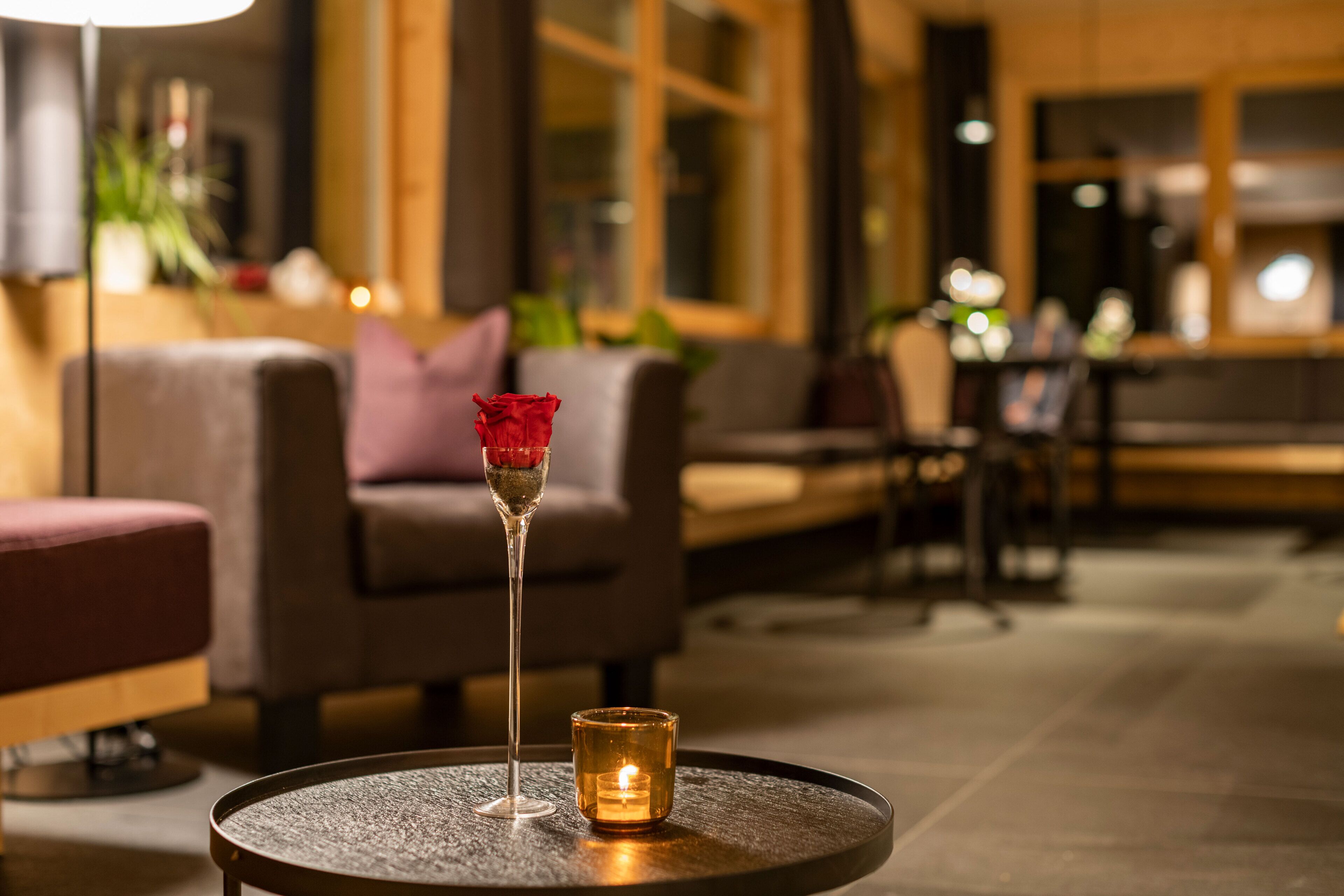 Ein gemütlicher Sitzbereich mit einem runden Tisch, einer Kerze und einem Glas mit einer Rose.