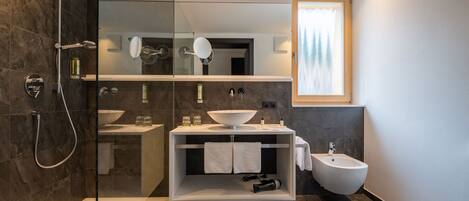 Un baño moderno con ducha de vidrio, lavamanos blanco y un bidé.