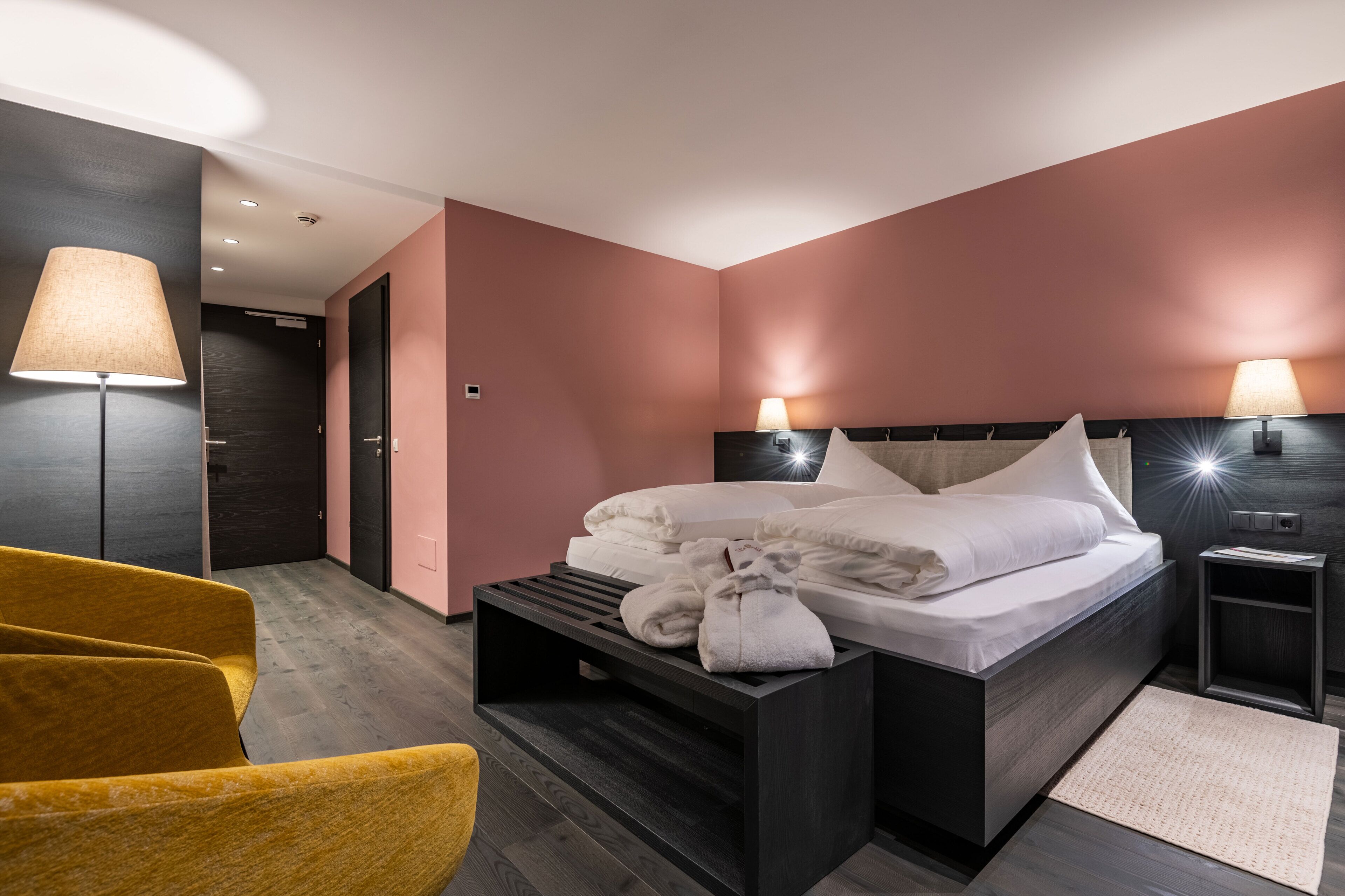 Ett modernt hotellrum med en säng, sänglampor, ett sängbord, en stol och en golvlampa.