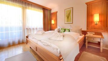 Habitación de hotel con una cama grande, cabecero de madera, dos lámparas de noche, una mesita de noche y una ventana con cortinas traslúcidas.