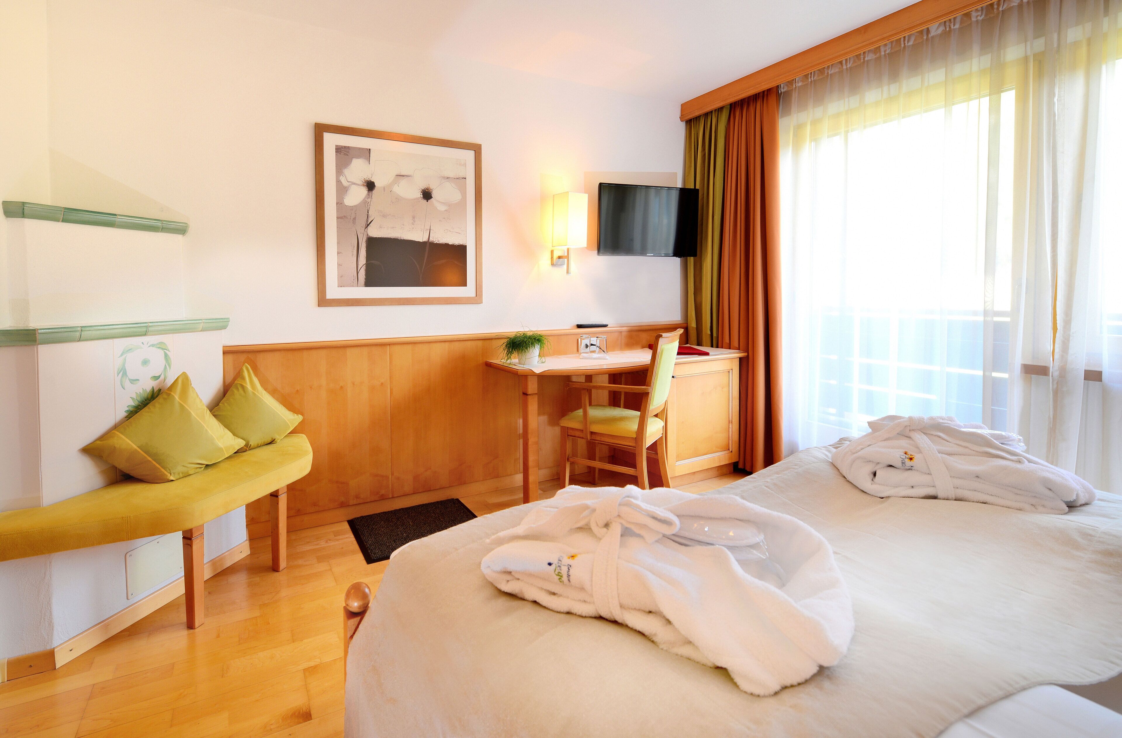 Habitación de hotel con cama, un banco, escritorio, silla, televisor y ventana con cortinas.