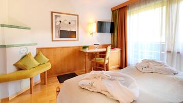 Habitación de hotel con cama, un banco, escritorio, silla, televisor y ventana con cortinas.