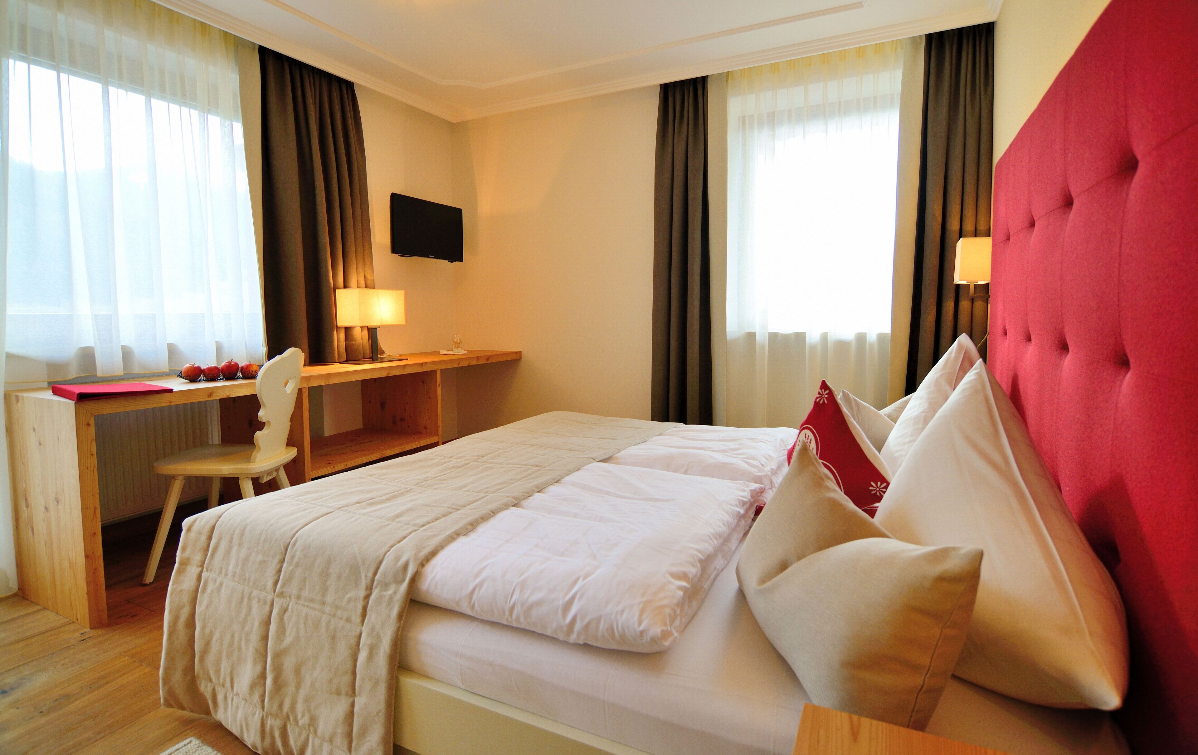 Ein Hotelzimmer mit Bett, Schreibtisch, Stuhl und einem Fernseher an der Wand.