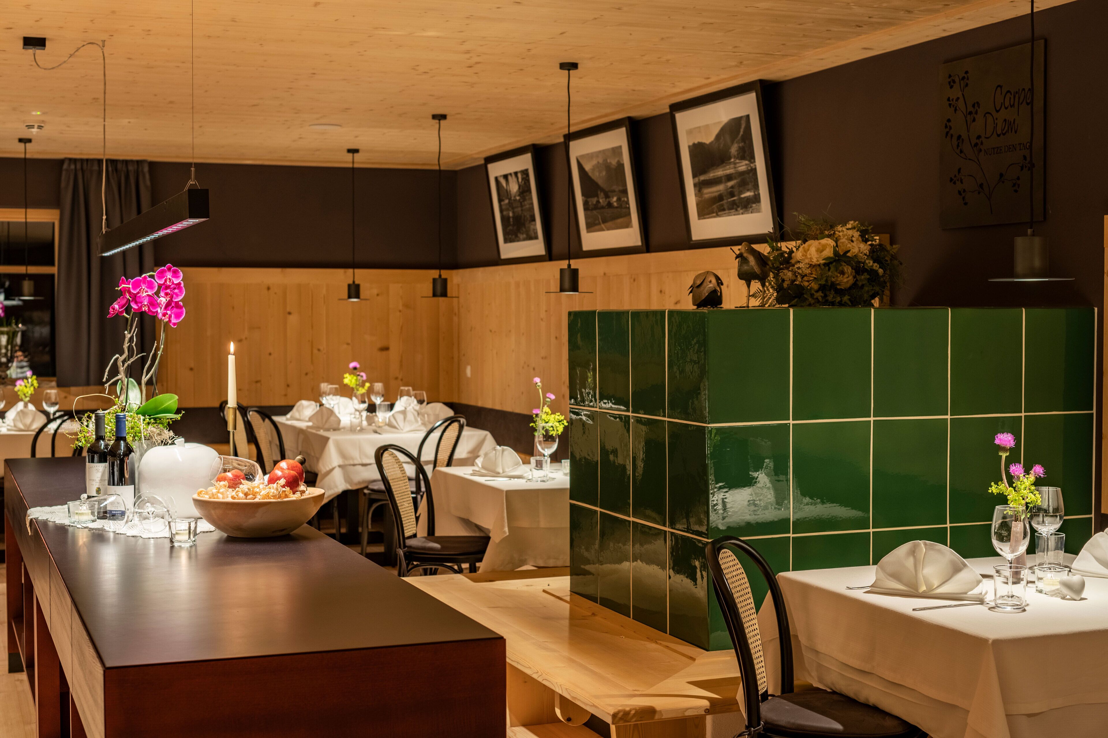 Un restaurant avec des murs lambrissés en bois, des murs recouverts de carreaux verts et des tableaux encadrés accrochés aux murs.
