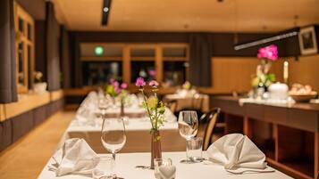 A restaurant with long tables set for dining, featuring white tablecloths, wine glasses, and small vases with flowers.