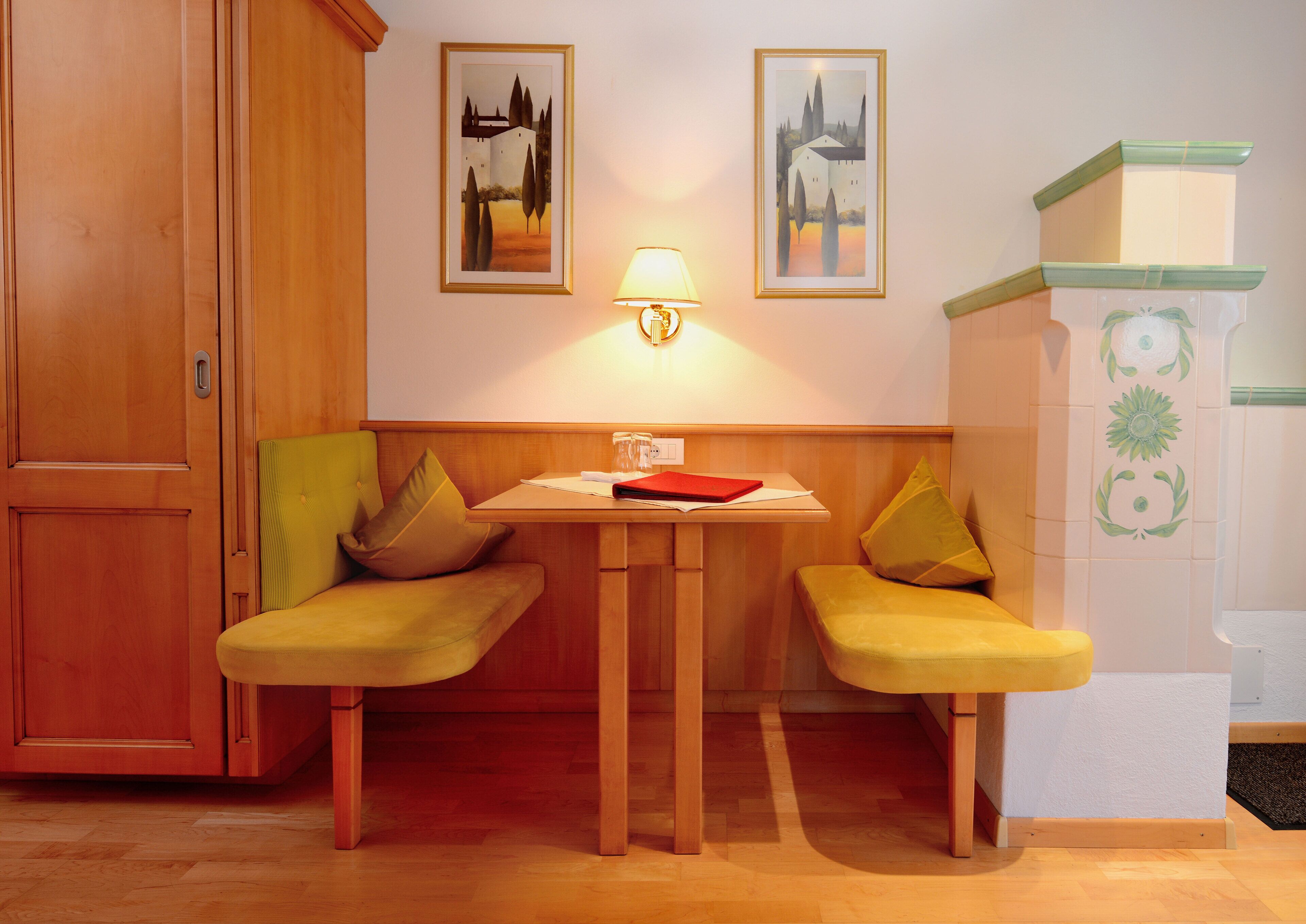 A room with a wooden cabinet, two yellow chairs, a table with a red folder, and two framed pictures on the wall.