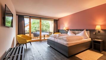 Ein modernes Hotelzimmer mit einem großen Bett, einem gelben Sessel, einem kleinen Tisch und Blick ins Freie durch eine Schiebetür.