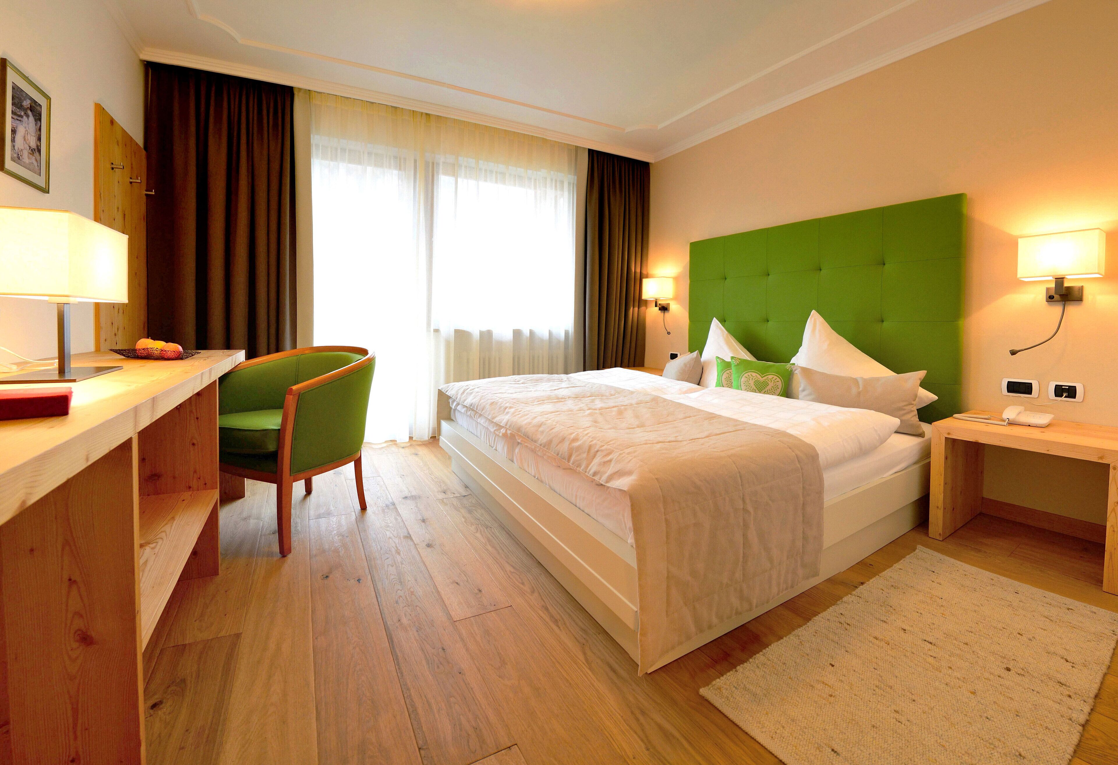 Una habitación de hotel con cama, escritorio, silla, lámpara y mesita de noche.