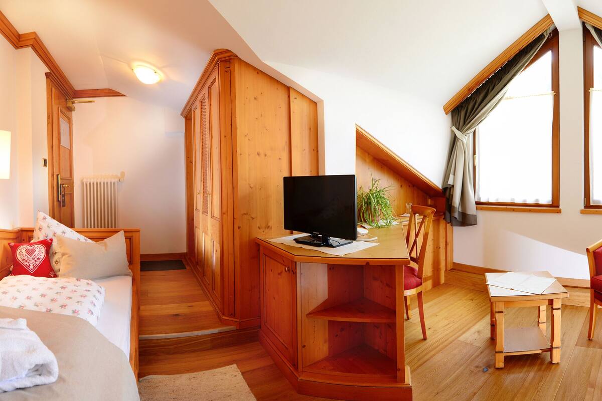 A bedroom with a bed, a desk with a computer, a chair, and a window with curtains.