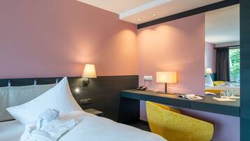 A hotel room with a bed, bedside table, lamp, chair, and a desk with a phone and glasses.