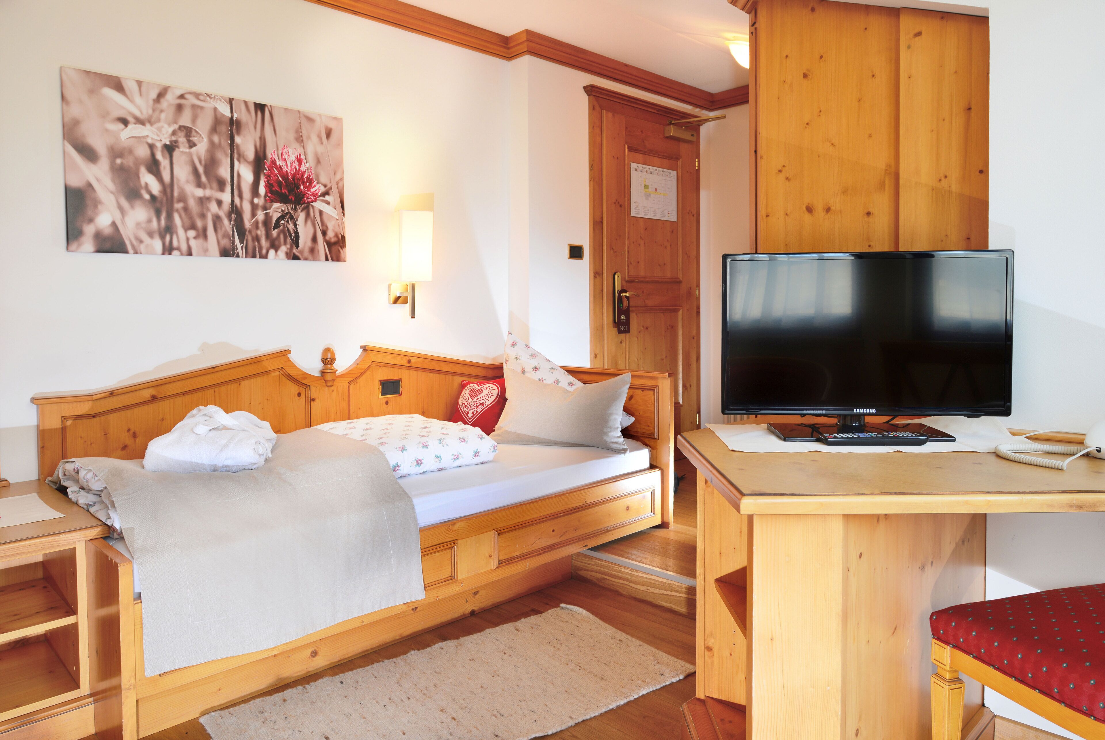 A wooden bed with a TV on a wooden desk, a red chair, and a wooden wardrobe.