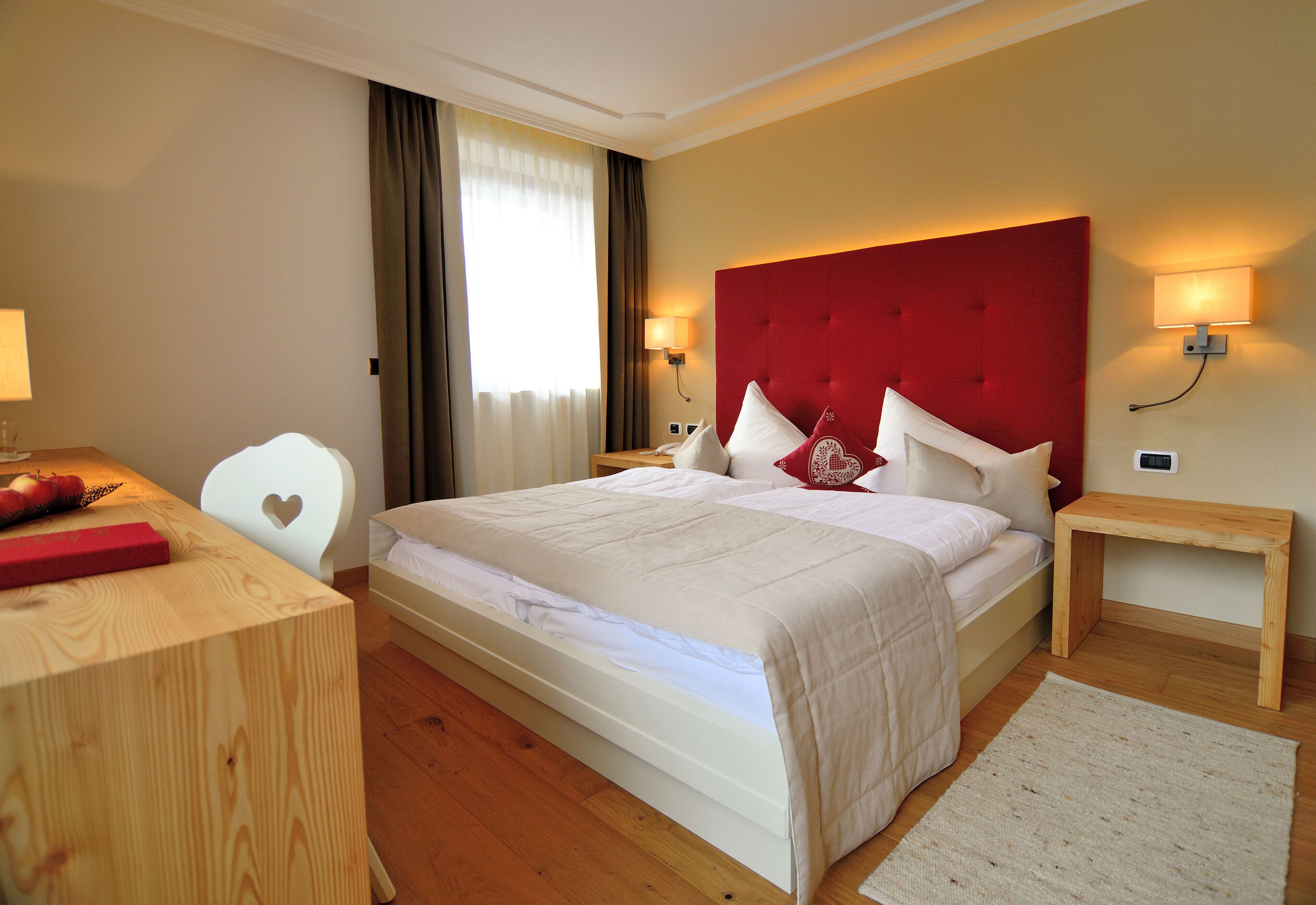 Una habitación de hotel con una cama grande, un escritorio, una silla, una mesita de noche y una mesilla auxiliar.