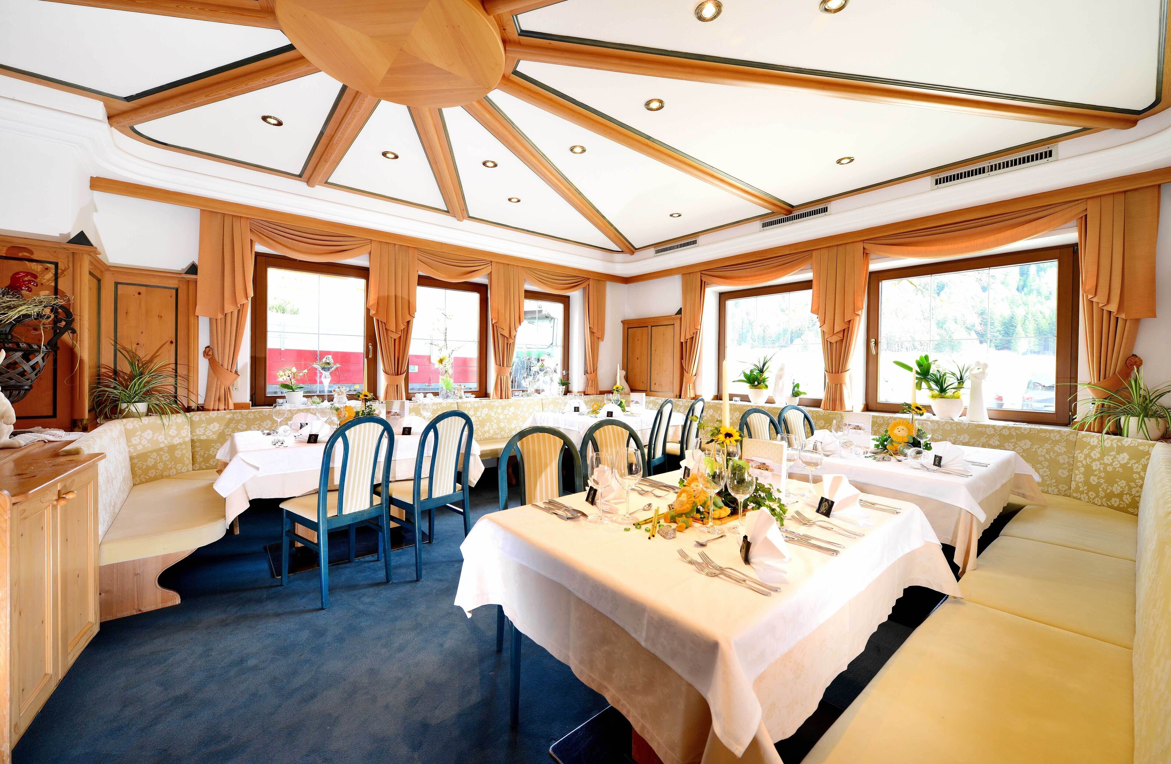 Uma sala de jantar com várias mesas preparadas para o serviço, janelas amplas e teto alto com vigas de madeira.