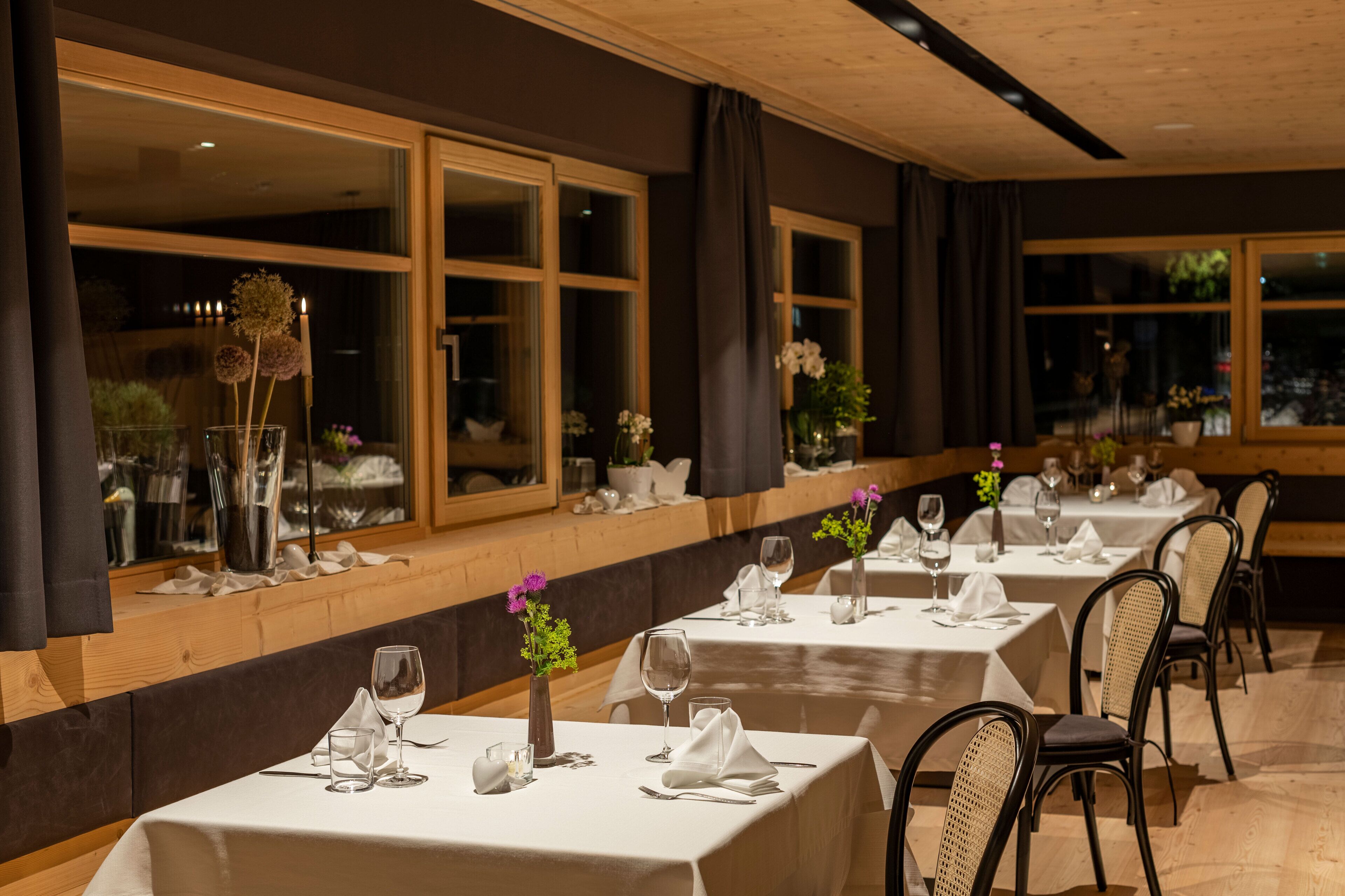 Un restaurant avec de nombreuses tables dressées pour le service, de grandes fenêtres et une vue sur l’extérieur.