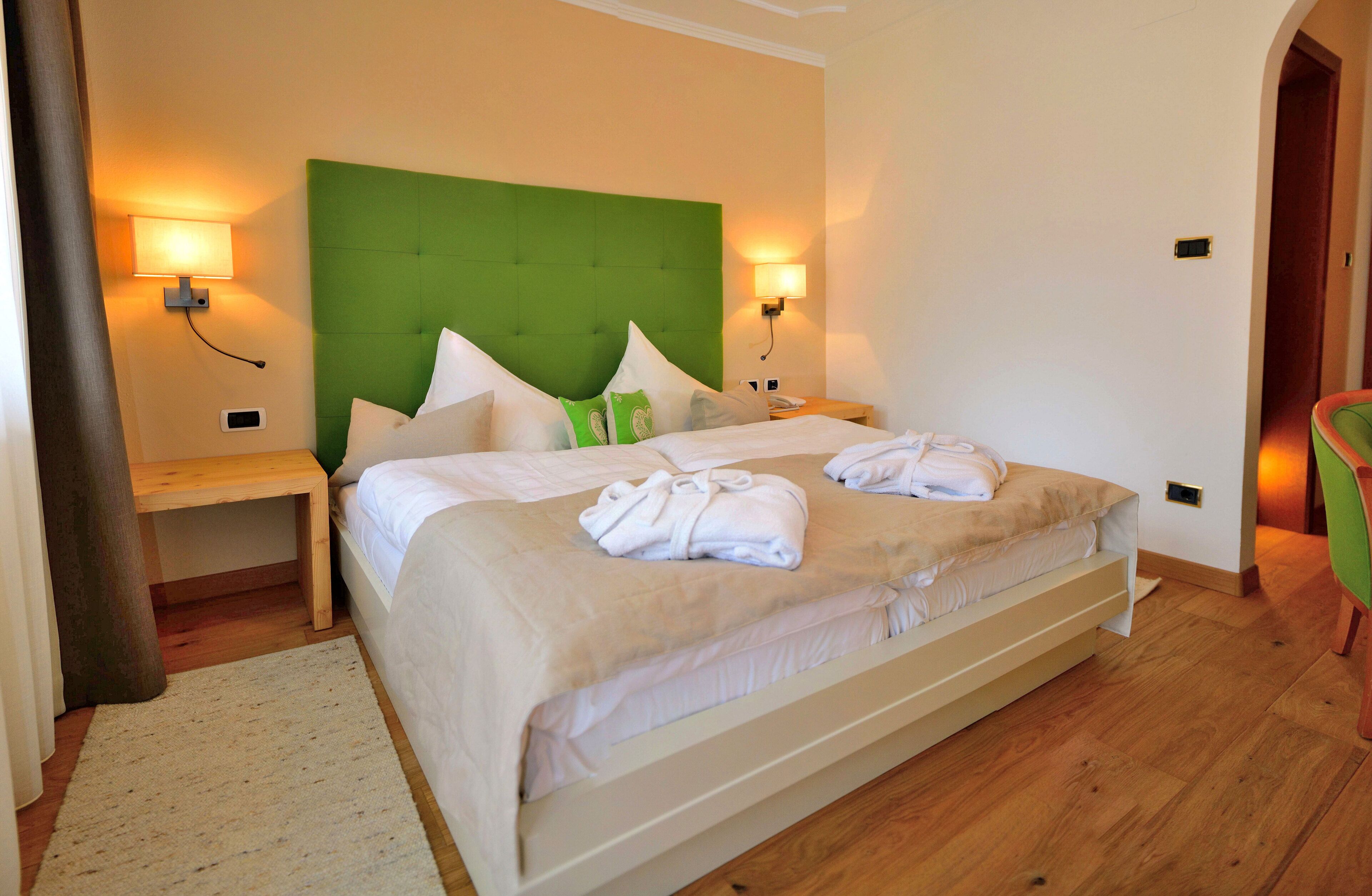 A double bed with a green headboard, two bedside tables, and a green chair.