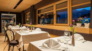 A restaurant with tables set for dining, large windows with a view of mountains, and a wooden ceiling.