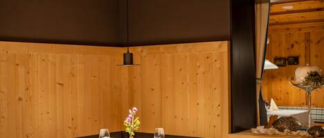 A dining area with a wooden paneled wall, a table set with white tablecloths, glasses, and a vase with flowers.