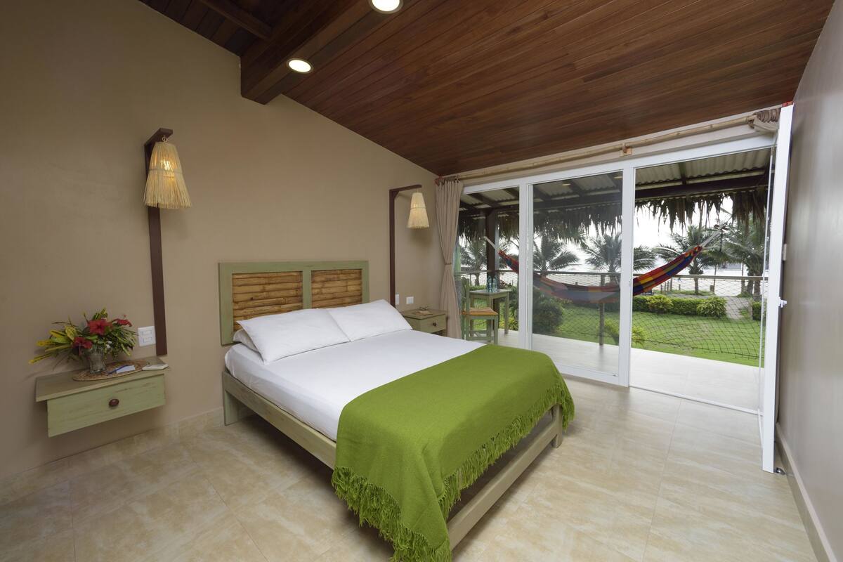 Un dormitorio con cama, mesita de noche, lámpara y vistas al exterior.
