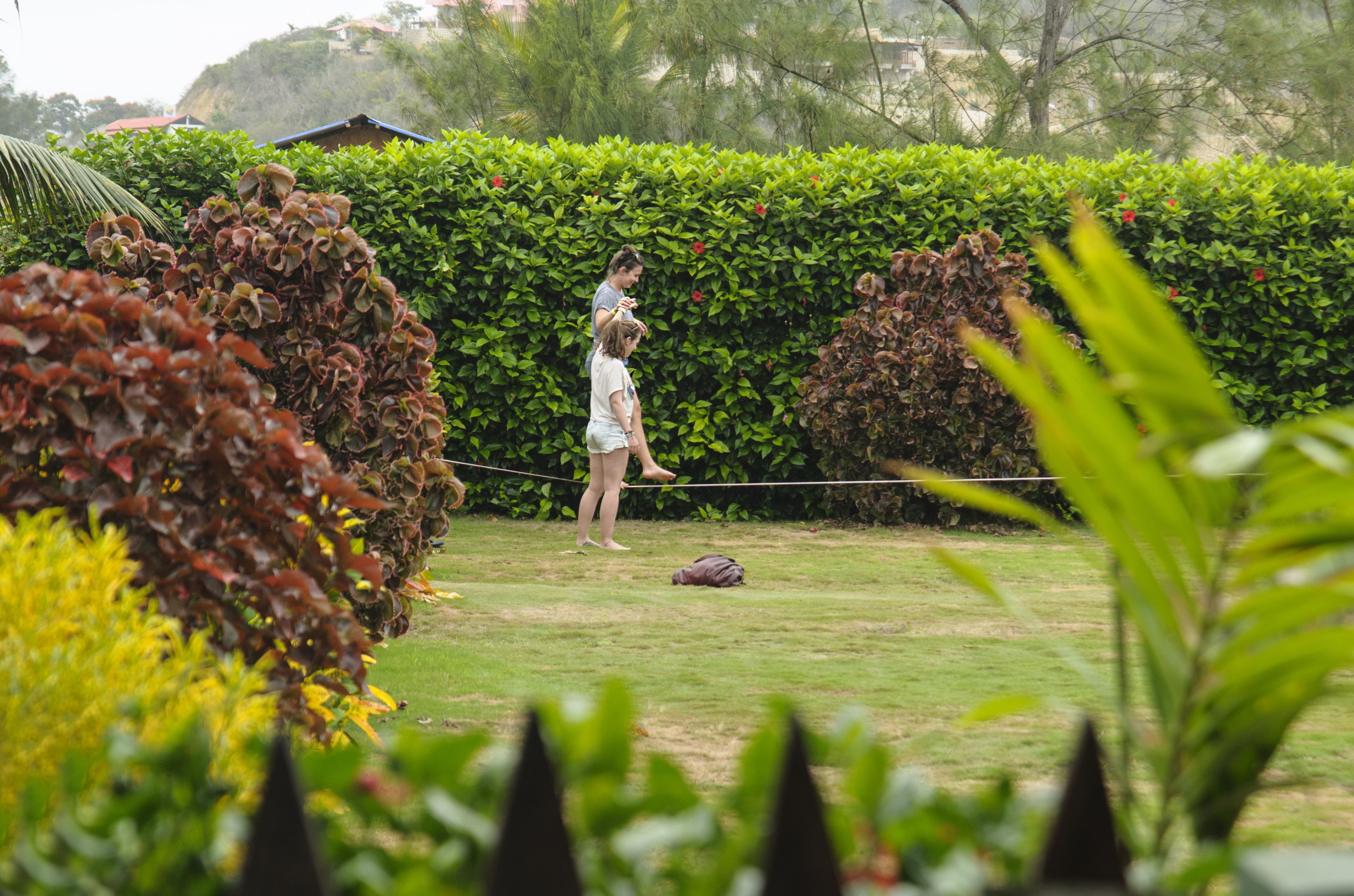 A person standing on a grassy area with a rope, surrounded by greenery and a hedge.