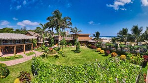 Un resort con edificios de techo de paja, un jardín cuidado y vista a la playa.