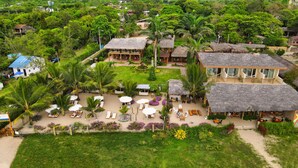 Vista aérea de un resort con edificios de techo de paja, zonas de estar al aire libre y exuberante vegetación.