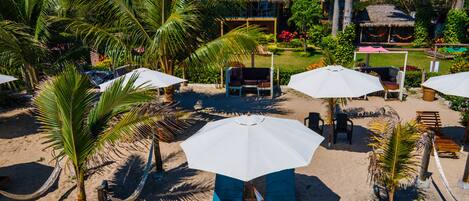 Un resort frente al mar con sillones de playa y sombrillas, palmeras y edificios con techo de paja.