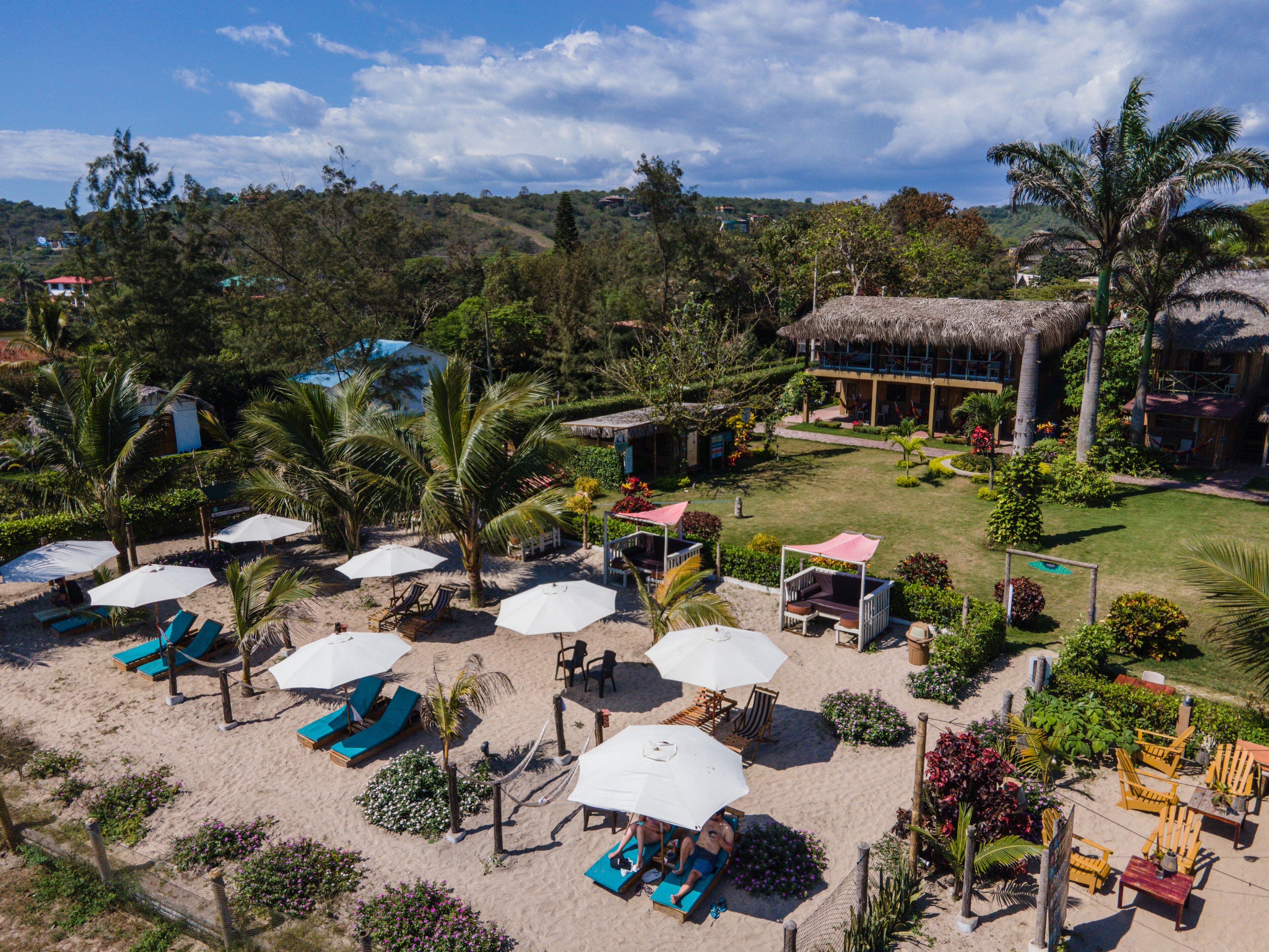 A beach resort with sun loungers, umbrellas, and a thatched-roof building.