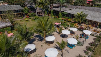 Un resort con edificios de techo de paja, palmeras y zonas de estar al aire libre con sombrillas.