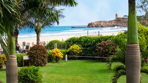 Vista costera con playa, palmeras y un acantilado rocoso.