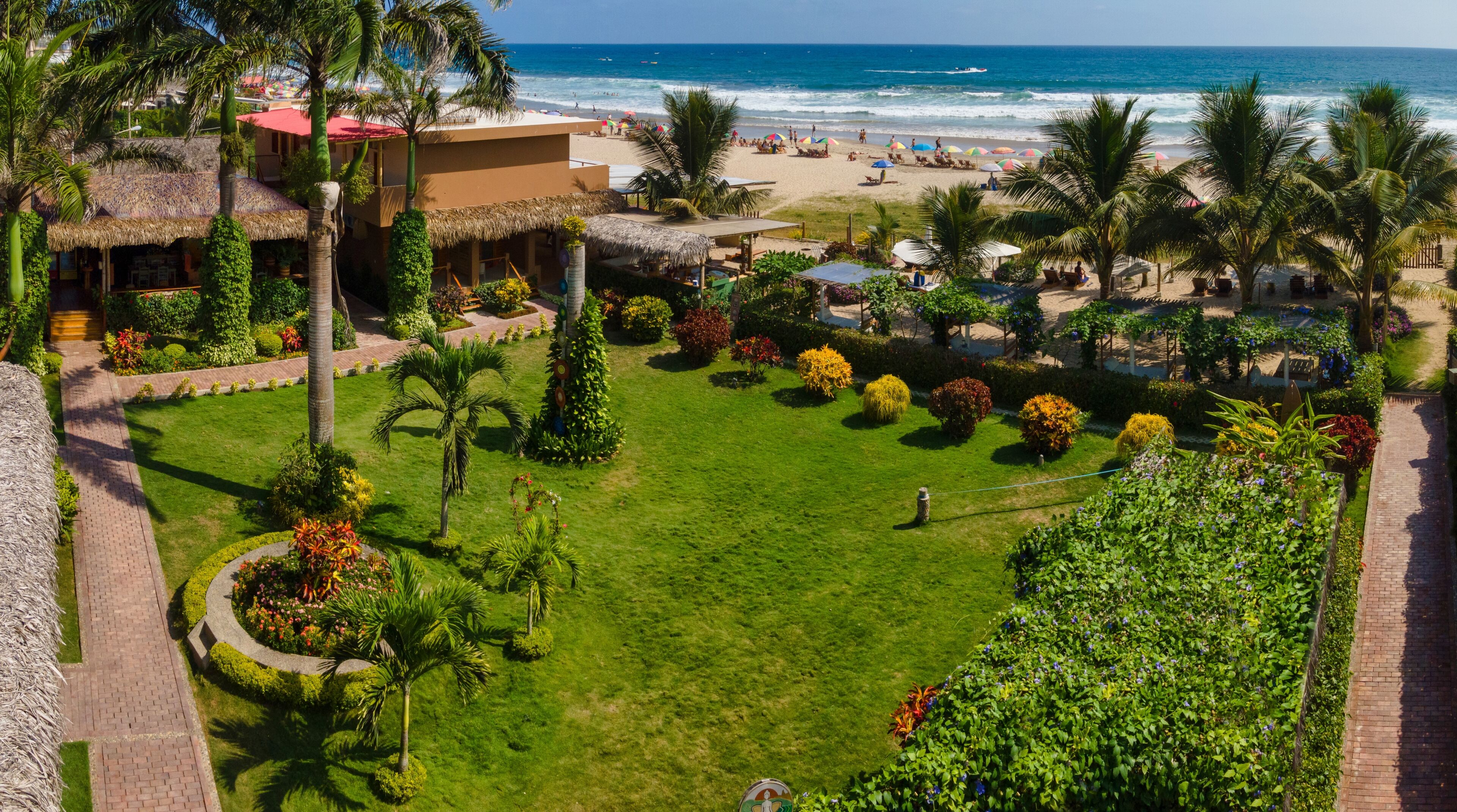 A tropical resort with a well-maintained lawn, palm trees, and a beach view.
