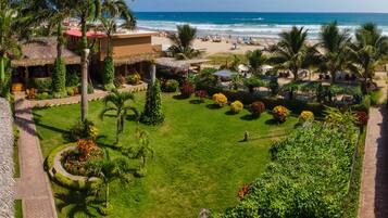 A tropical resort with a well-maintained lawn, palm trees, and a beach view.