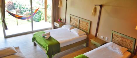 A hotel room with two beds, a window with a view of greenery, and a hammock outside.