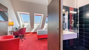 Habitación de hotel con alfombra roja, un escritorio con silla, cama y baño con azulejos negros.