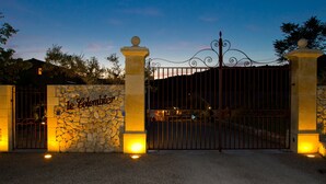 A gated entrance with a stone wall and a metal gate, illuminated by ground lights. - Hôtel Le Colombier (Moustiers-Sainte-Marie)